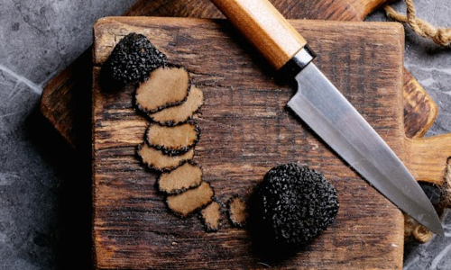 Black perigord truffle slices sitting on a dark wooden cutting board beside a chef's knife