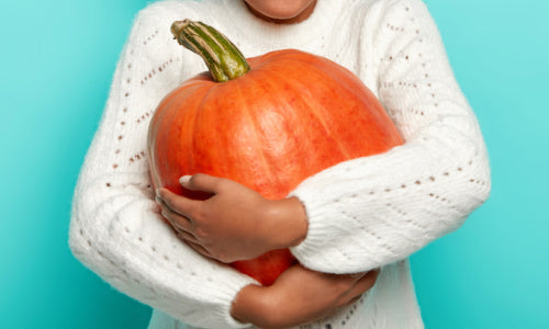 Woman in a white sweater hugging a pumpkin